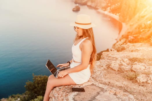 Freelance women sea working on the computer. Good looking middle aged woman typing on a laptop keyboard outdoors with a beautiful sea view. The concept of remote work