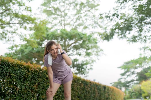 Asian woman taking a moment to catch her breath after tired workout in park.