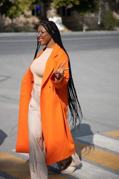 Kazakhstan, Shymkent - September 04 2023: Cheerful African woman . Long haired brunette lady in orange coat smiles and walks outdoors