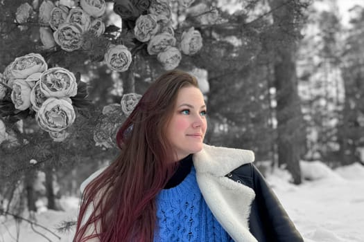 long-haired smiling brunette girl with blue eyes in a blue sweater against the background of a black and white winter forest.