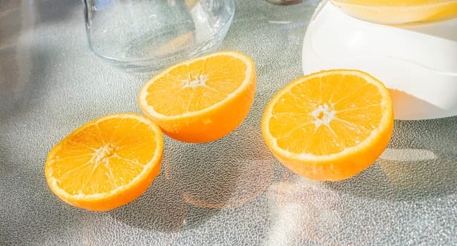 Vibrant orange halves glisten in sunlight, adjacent to a clear juicer