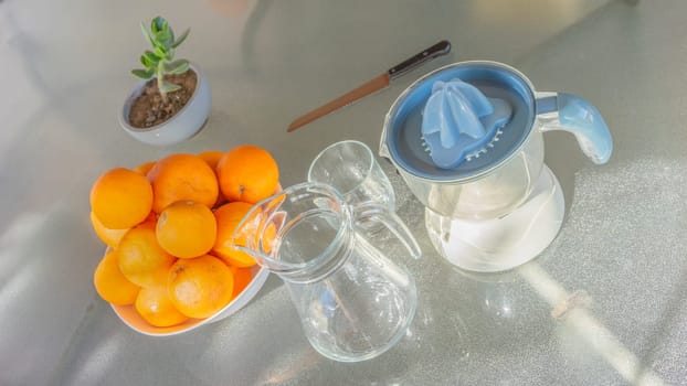 A bowl of ripe oranges, a juicer, and empty glasses await to create fresh juice, hinting at a healthy, refreshing beverage preparation