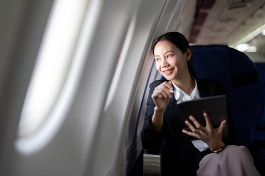 Successful young asian business woman sits in airplane cabin plane and working from anywhere. Flying at first class.