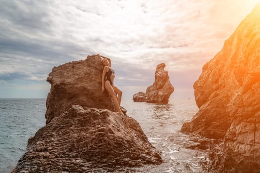 Woman swimsuit sea. Attractive blonde woman in a black swimsuit enjoying the sea air on the seashore around the rocks. Travel and vacation concept