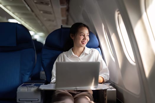 Successful young asian business woman sits in airplane cabin plane and working from anywhere. Flying at first class.