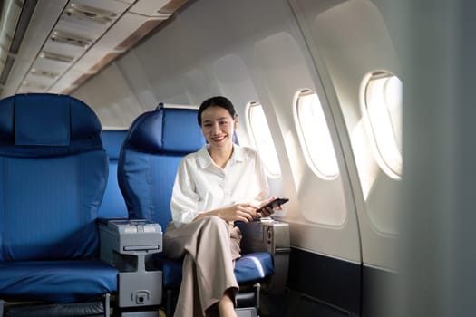 Traveling and technology. Flying at first class. Young business woman passenger using smartphone while sitting in airplane flight.