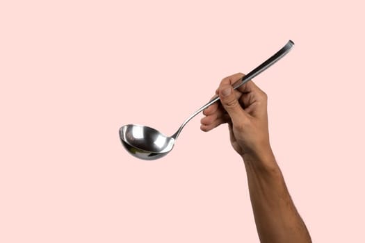 Black male hand holding a silver kitchen ladle isolated on pink background. High quality photo