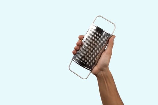 Black male hand holding a kitchen grater on cyan background. High quality photo