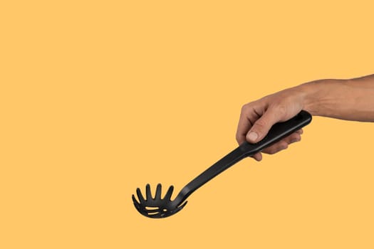 Black male hand holding plastic kitchen skimmer on yellow background. High quality photo