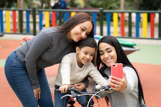 Happy smiling lesbian mothers taking a selfie with their son in a playground.