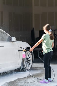 Denver, Colorado, USA-September 1, 2023-A young girl enthusiastically assists in washing the family's electric car in their suburban driveway.