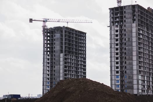building cranes at the background of a multi-storey building under construction. New houses for families
