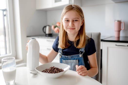 Sweet Girl Looks Into The Frame Sitting At Kitchen Table With Dry Breakfast In Plate