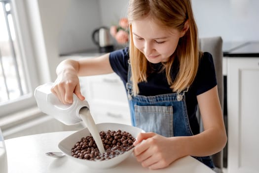 Sweet Girl Pours Milk Into Bowl With Dry Breakfast In Kitchen