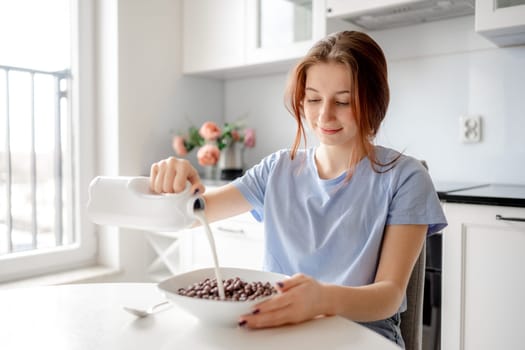 Sweet Teenage Girl Pours Milk Into Bowl With Dry Breakfast In Kitchen