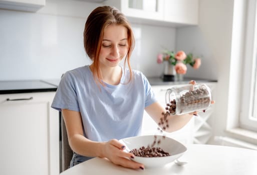 Sweet Teenage Girl Pours Cereal Into Plate For Breakfast In Kitchen