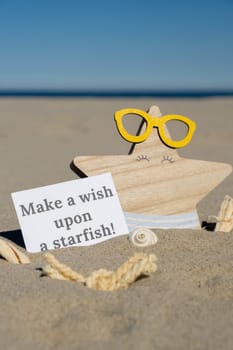 MAKE A WISH UPON A STARFISH text on paper greeting card on background of funny starfish in glasses summer vacation decor. Sandy beach sun coast. Holiday concept postcard. Getting away Travel Business concept