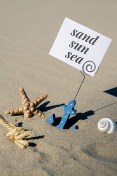 SAND SUN SEA text on paper greeting card in anchor paper holder and starfish seashell summer vacation decor. Sandy beach sun coast. Holiday concept postcard. Getting away Travel Business concept