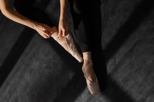 Faceless ballerina sits on the floor and puts on pointe shoes. Top view