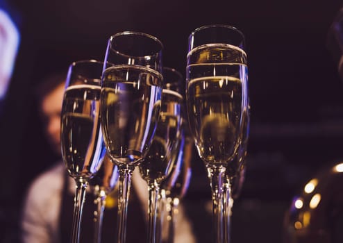 Many glasses with champagne lit by nightclub lights on dark background