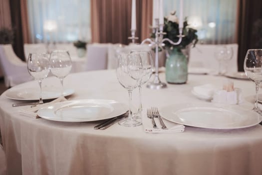 restaurant interior. White table setting. Elegant empty plate, cutlery, napkin and glasses for vine.