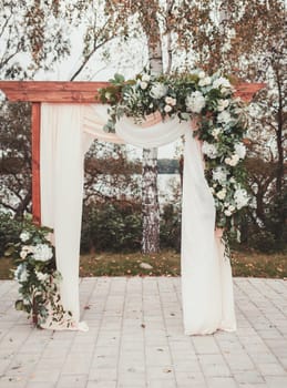 Wedding arch decorated with cloth and flowers outdoors. Beautiful wedding set up. 