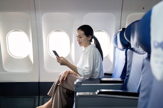 A woman is sitting on an airplane and looking at her phone. She is smiling and she is enjoying her time on the plane