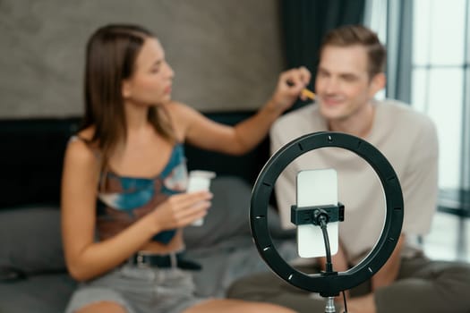 Young woman making beauty and cosmetic tutorial video content for social media using her boyfriend as model and light ring. Beauty blogger showing how to beauty care to audience or follower. Unveiling