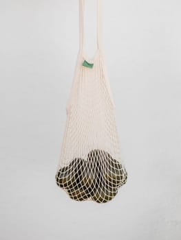 A Net Bag Filled With A Bunch Of avocado on white background.