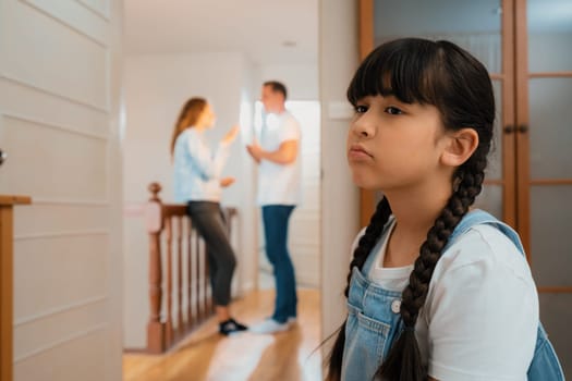 Stressed and unhappy young girl huddle in corner crying and sad while her parent arguing in background. Domestic violence at home and traumatic childhood develop to depression. Synchronos