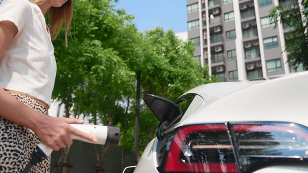 Young woman recharge EV electric car battery at residential area EV charging station in urban city condo with sustainable green and renewable clean energy lifestyle for electric vehicle innards