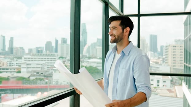 Professional architect engineer or male worker in casual outfit looking at skyscraper and city view while holding project plan. Creative design, civil engineering, building construction. Tracery