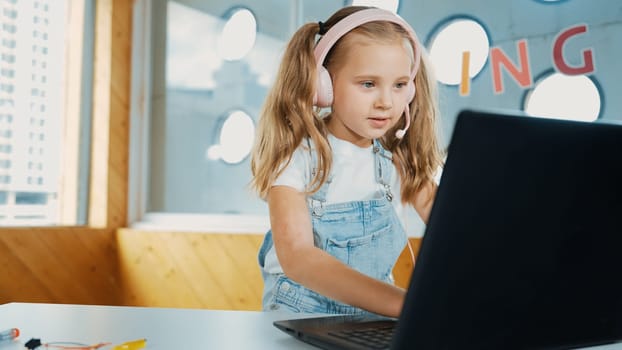 Young student working on laptop or studying in online classroom. Caucasian girl typing on laptop while doing homework or listening music.Little kid wearing headphone. Creative learning. Erudition.
