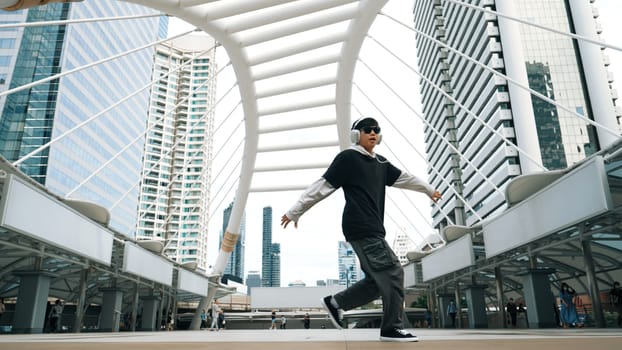 Young asian hipster show footstep at city center surround by people. Stylish fashion street dancer perform B-boy or freestyle dancing with low angle. Outdoor sport 2024. Break dancing. Sprightly.