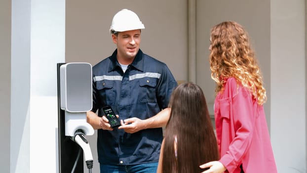 Technician install home EV charging station, providing service support for EV app on customer smartphone for monitoring charging status and set charging schedules at home. Panorama Synchronos