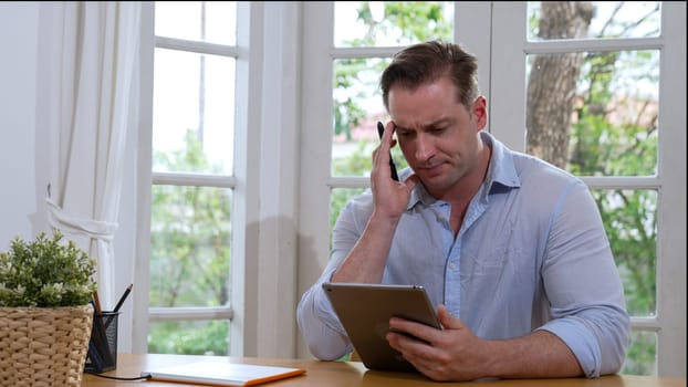 Businessman struggle to solve work problem from home using laptop, sitting on his desk at home office with stressed and frustrated expression, trying to figure out solution for problem. Synchronos