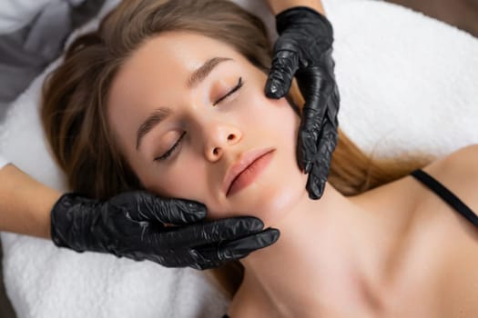 Top view of womans hands massaging female client facial skin at beauty salon
