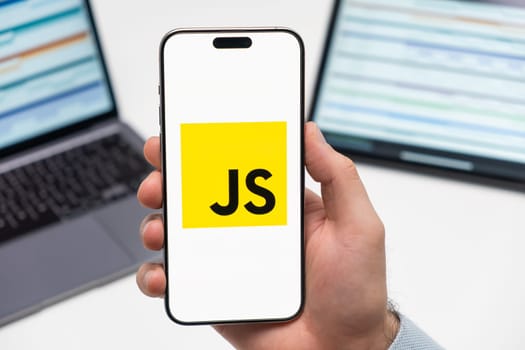 PRAGUE, CZECH REPUBLIC - JANUARY 21 2024: JS logo on the screen of smartphone in mans hand on the workplace background.