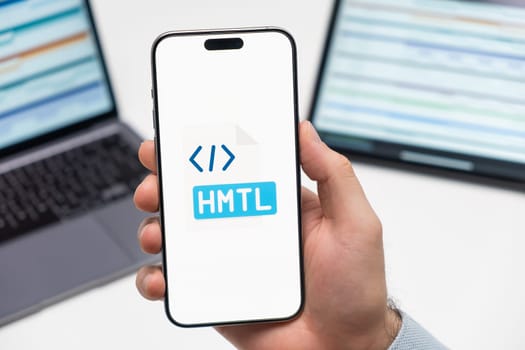 PRAGUE, CZECH REPUBLIC - JANUARY 21 2024: HTML logo on the screen of smartphone in mans hand on the workplace background.