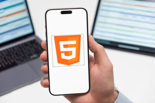 PRAGUE, CZECH REPUBLIC - JANUARY 21 2024: HTML logo on the screen of smartphone in mans hand on the workplace background.