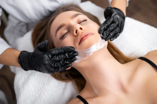 Enjoying a rejuvenating experience, a beautiful young woman receives a face lifting massage at the beauty salon.