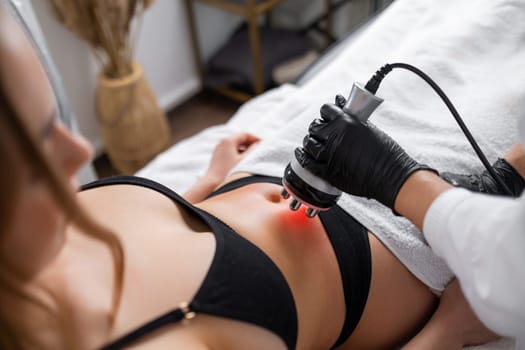 A cosmetologist in a beauty clinic performs RF skin tightening and body contouring on a young womans abdomen.