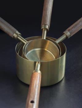 Set of Brass Measuring Cups with Wood Handles with Hanging Hole Design on dark background. Wooden & Brass Measuring Cups & Spoons for Measuring Dry and Liquid Ingredients, Kitchen tool, Space for text, Selective Focus.