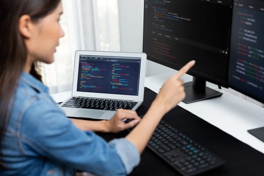 Young Asian girl of IT developer pointing online information on pc with coding program data application on website project, wearing jeans shirt. surrounded by safety programing two screens. Stratagem.