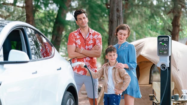 Outdoor adventure and family vacation camping in nature travel by eco friendly car for sustainable future. Lovely family recharge EV car with EV charging station in campsite. Perpetual