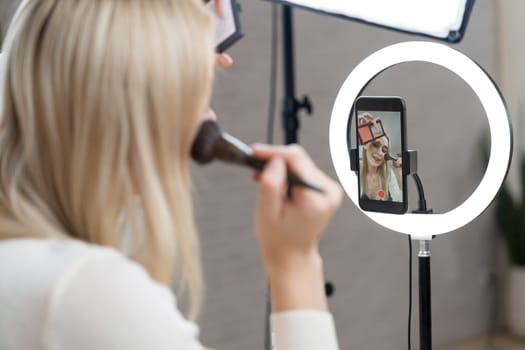 Rear view young woman making beauty and cosmetic tutorial video content for social media. Beauty blogger showing how to apply beauty care to audience or follower on camera screen. Blithe