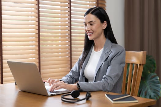 Female call center operator or customer service helpdesk staff working on workspace while talking on the headset to provide assistance for customer. Professional modern business service. Blithe