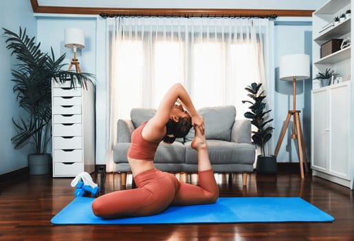 Flexible and dexterity woman in sportswear doing yoga position in meditation posture on exercising mat at home. Healthy gaiety home yoga lifestyle with peaceful mind and serenity.