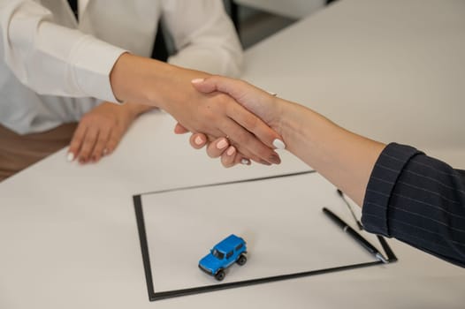 Car purchase deal. Seller and female buyer shaking hands