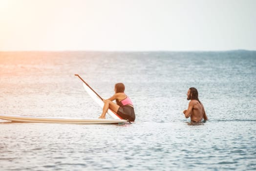 Sea woman and man on sup. Silhouette of happy young woman and man, surfing on SUP board, confident paddling through water surface. Idyllic sunset. Active lifestyle at sea or river